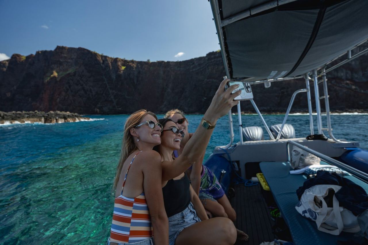 Two guests taking a photo from the raft beneath the sea cliffs of Lānaʻi