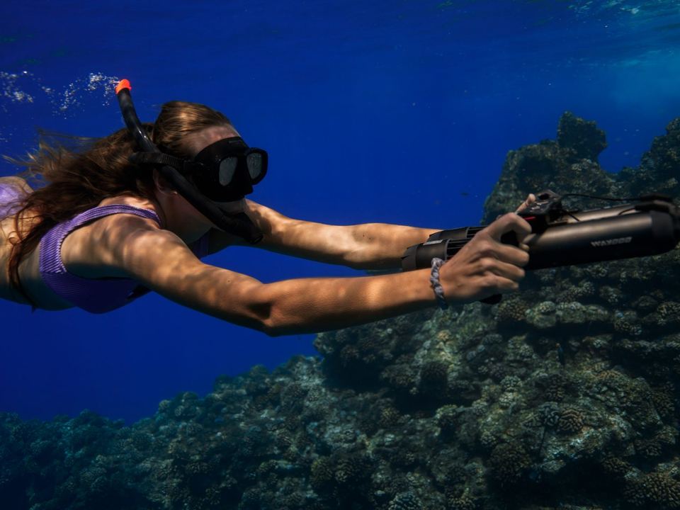 A snorkeller riding a sea scooter above a coral reef off Lānaʻi
